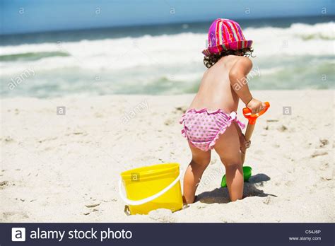 Rear View Of A Girl Digging With A Sand Shovel On The Beach Stock Photo