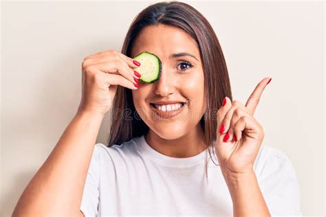 Young Beautiful Brunette Woman Holding Slice Of Cucumber Smiling Happy