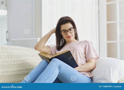 A Girl With Glasses Sitting On A Sofa Reading A Book Stock Image