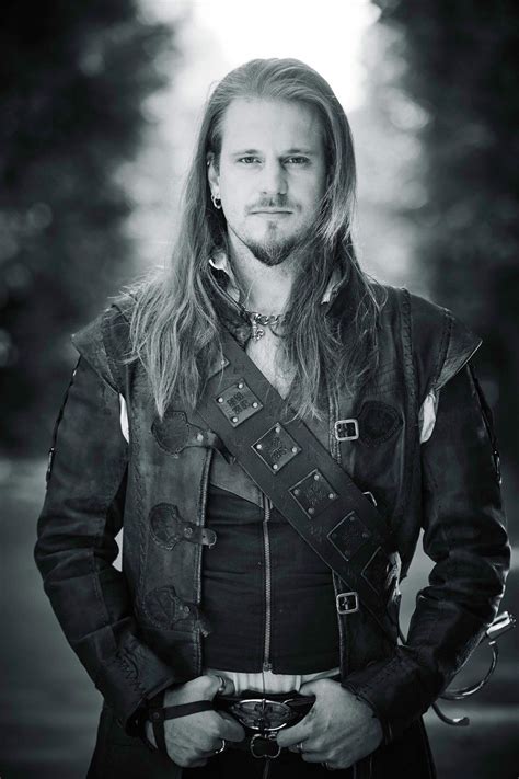A Man With Long Hair Wearing A Leather Jacket And Holding His Hands In His Pockets