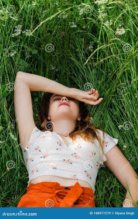 Close Up Of Young Brunette Girl In White Top And Red Skirt Lying Down In Green Meadow Field