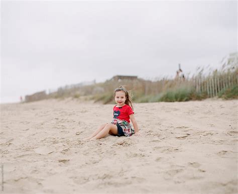 Cute Young Girl Sitting On A Beach In Windy Weather By Stocksy Contributor Jakob Lagerstedt