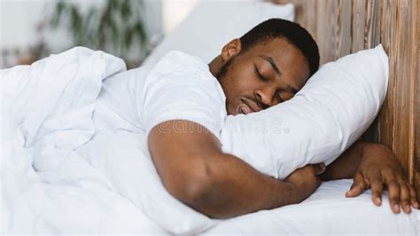 African Man Sleeping Hugging Pillow Lying In Bed At Home Stock Photo