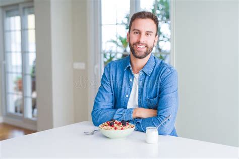 Handsome Man Eating Cereals For Breakfast At Home With A Happy And Cool Smile On Face Stock
