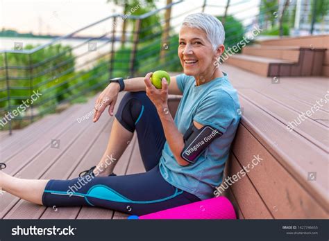 Sporty Woman Eating Apple Beautiful Woman With Gray Hair In The Early Sixties Relaxing After