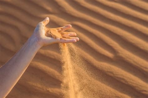 premium photo sand slipping through the fingers of a woman s hand in the desert