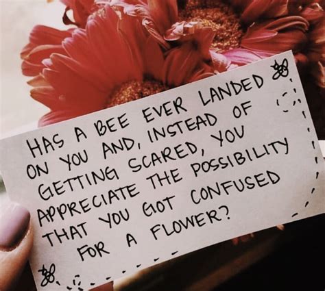 A Person Holding A Note With Flowers In The Background That Reads Has