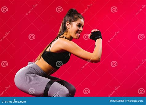 A Girl With A Pumped Up Figure Squats With A Resistance Elastic Band Looking To The Side