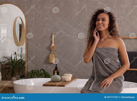 Beautiful African American Woman Sitting On Edge Of Tub In Bathroom
