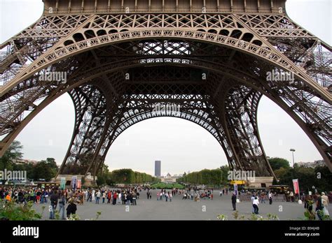 Eiffel Tower Base With Tourists And Sightseers Gathering And Queuing To