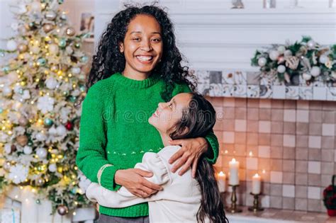 Mom And Daughter Hug Standing Against Christmas Tree Stock Photo