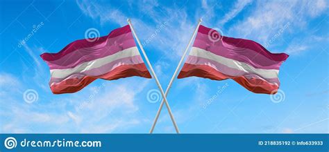 Two Crossed Lesbian Pride Flags Waving In The Wind On Flagpole Against The Sky With Clouds On