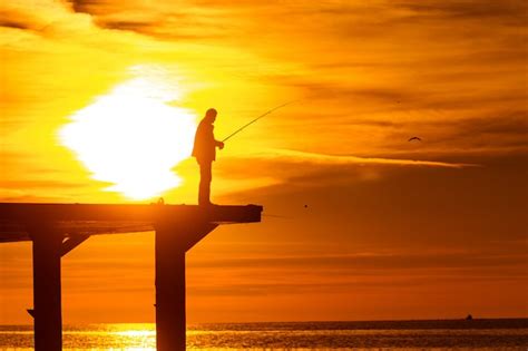 Premium Photo Fisherman Fishing In The Sea On The Pier At Sunset