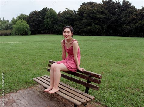 Portrait Of Young Asian Woman Sitting On Bench On Grass Field With