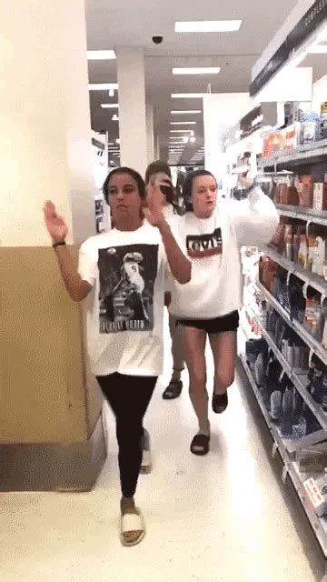 two girls are walking down the aisle of a grocery store and one girl is holding her hand up
