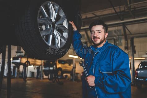 Auto Mechanic With Wrench Stands Near A Car On A Lift Car Repairman In