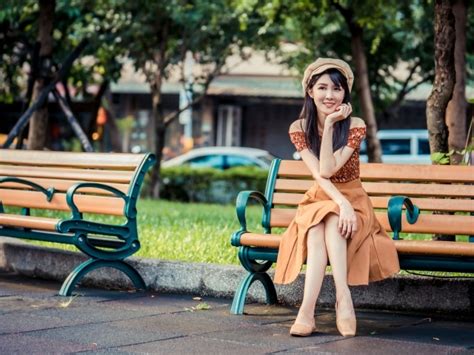 Красивая улыбающаяся азиатка сидит на лавке в парке обои для рабочего