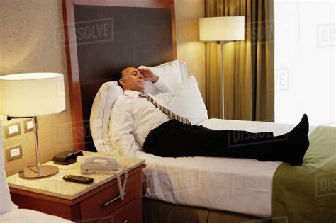 Middle Aged Businessman Laying On Bed In Hotel Room Stock Photo
