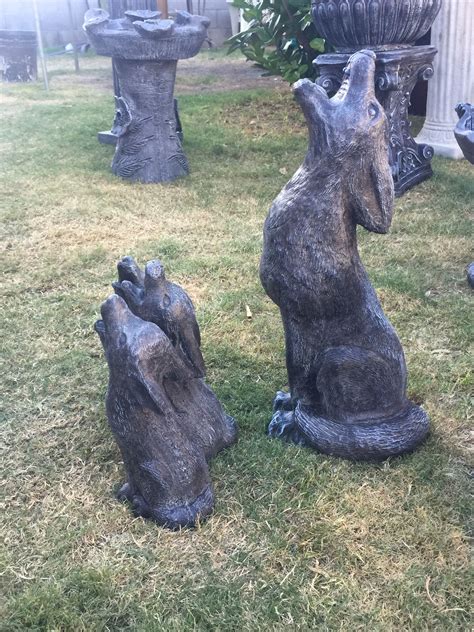 A Statue Of A Dog Sitting In The Grass Next To Two Stone Statues On