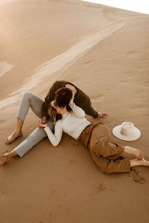 A Man And Woman Laying On The Ground In The Sand With Their Arms Around