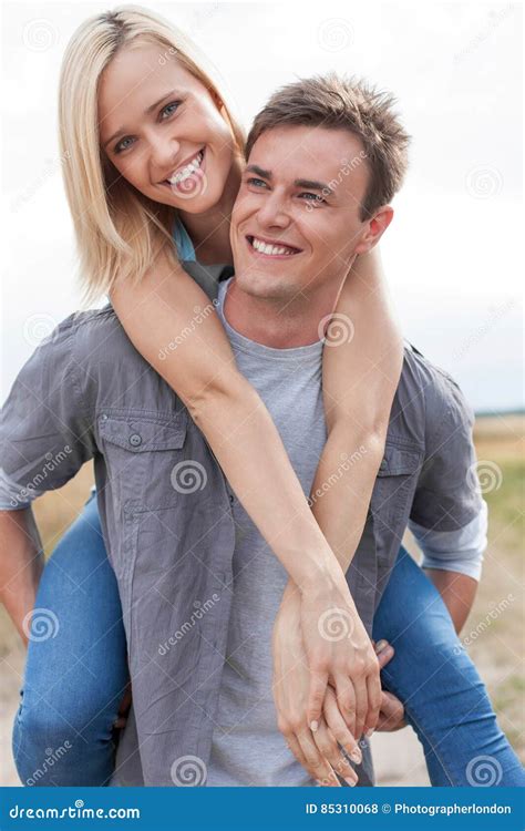 Happy Young Man Giving Piggyback Ride To Girlfriend On Field Stock
