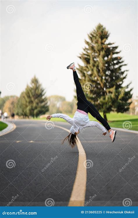 Woman Athlete Leaping Somersault On The Road Doing Exercises Outdoors
