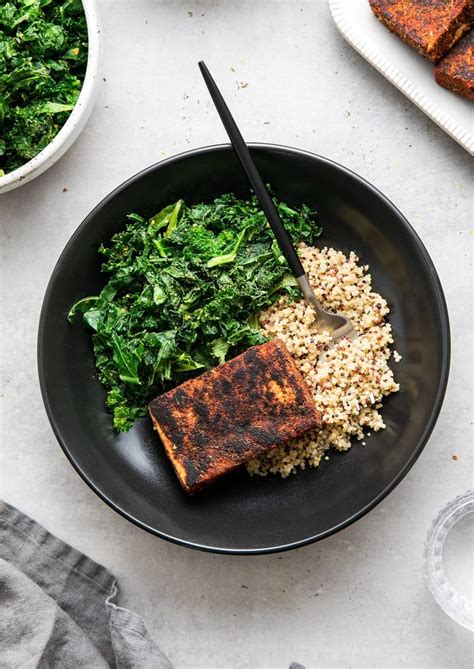 A Black Plate Topped With Rice Greens And Tofu