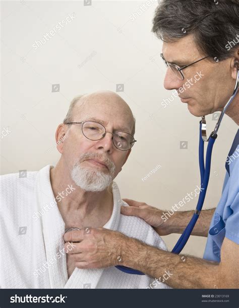 Male Doctor Or Nurse In Blue Scrubs Listening To Senior Mans Heart