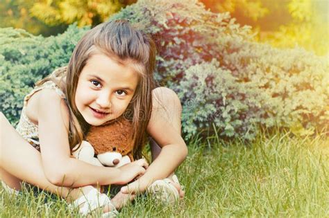 Cute Smiling Little Girl Holding Teddy Bear And Sitting On The G Stock
