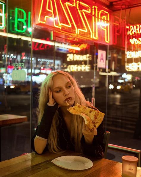 A Woman Sitting At A Table Eating A Slice Of Pizza With Neon Signs In