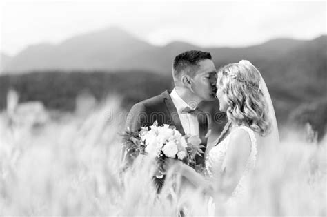 Groom Hugging Bride Tenderly And Kisses Her On Forehead In Wheat Field