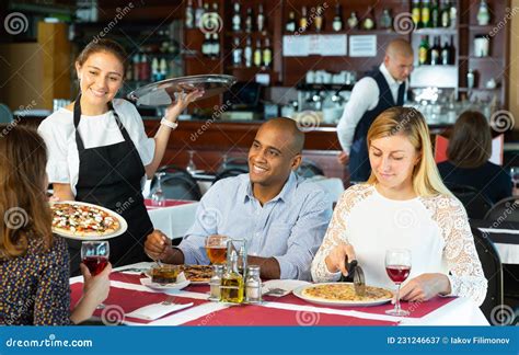 Hispanic Waitress Serving Pizza To Friendly Company In Restaurant Stock