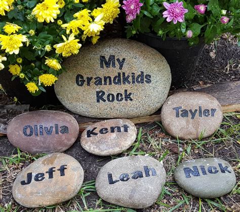 Four Rocks With Names Written On Them Sitting In Front Of Some Flowers