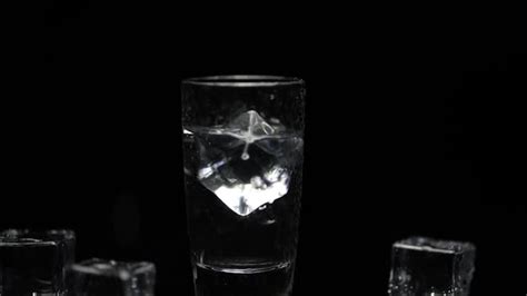 Add Ice Cube To Shot Of Vodka In Glass Against Black Background