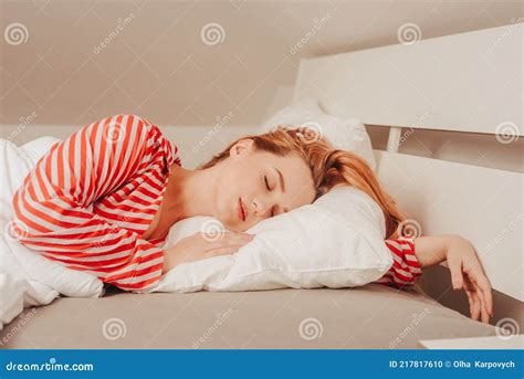 A Beautiful Girl On A White Bed In Red Striped Pajamas Is Sleeping