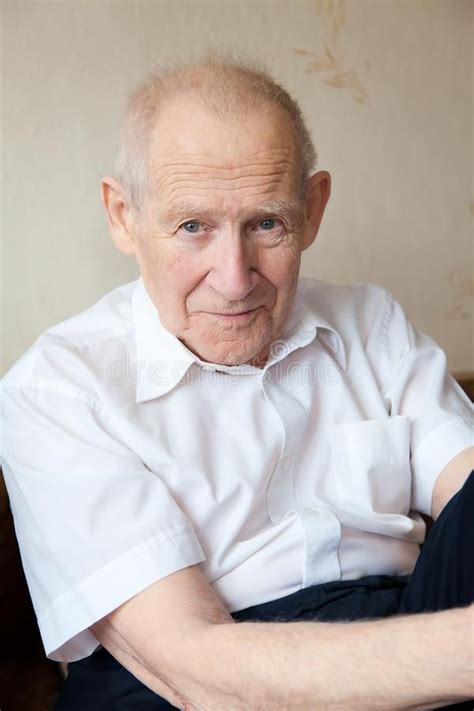 an old man sitting on a couch with his arms crossed and looking at the camera