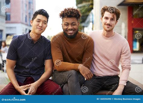 Three Millennial Male Hipster Friends On A Bench In A City Street Smiling To Camera Close Up