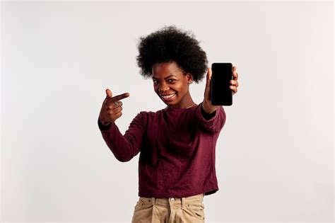 Une Fille Afro Américaine En Pull Marron Pose En Pointant Vers Son Téléphone Intelligent