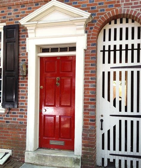 A Red Door With Black Shutters Is In Front Of A Brick Wall And White Trim