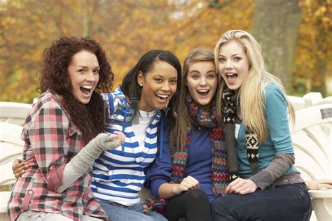 Group Of Four Teenage Girls Sitting On Bench In Autumn Park By Omg