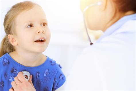 Доктор осматривает маленькую девочку с помощью стетоскопа счастливый улыбающийся ребенок