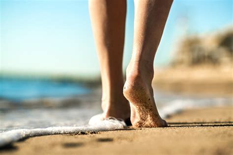 premium photo close up of woman feet walking barefoot on sand leaving footprints on golden