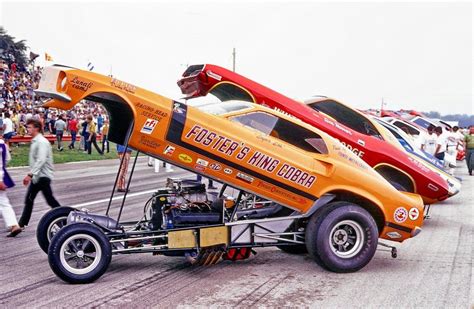 an orange race car with two engines on it s flatbed is parked in front of other cars