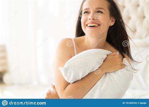 Positive Woman With Pillow Sitting In Bed And Smiling To Camera At Home