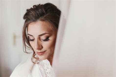 Premium Photo Gorgeous Bride In Silk Robe Holding Stylish Wedding Dress In Room In The Morning