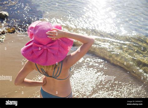 fröhliches junges wunderschönes mädchen in badeanzug und pinkfarbenem hut steht an der küste