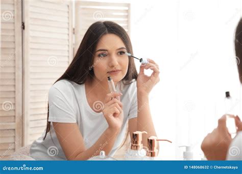 Beautiful Woman Applying Oil Onto Her Eyelashes Near Mirror Stock Photo