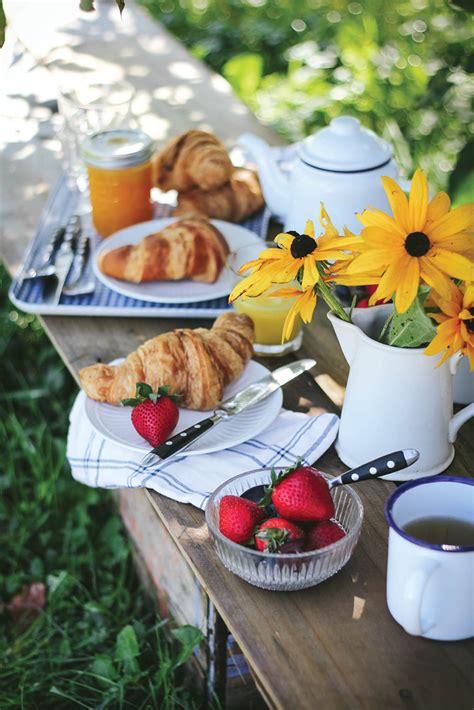 Two Plates With Strawberries And Croissants Sit On A Picnic Table In