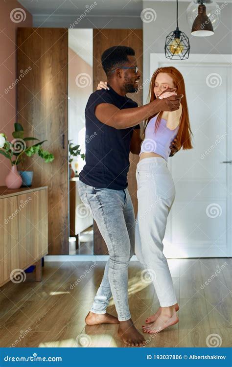 Lovely Young Multiethnic Couple Dance In Living Room Stock Photo