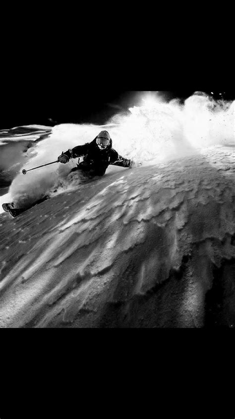 A Man Riding Skis Down The Side Of A Snow Covered Slope In Front Of A